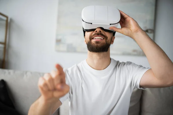 Smiling bearded man in vr headset pointing with finger during gaming at home — Stock Photo