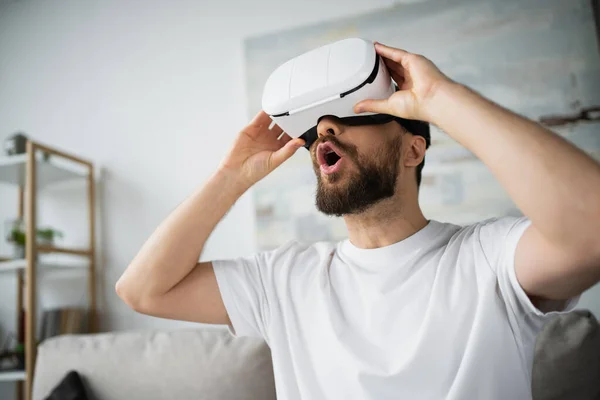 Шокированный босоногий мужчина настраивал гарнитуру VR во время игры дома — стоковое фото