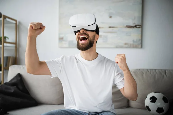 Amazed and bearded man in vr headset rejoicing while gaming in living room — Stock Photo