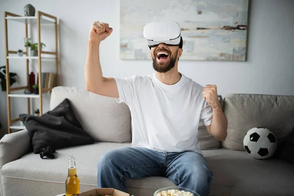 KYIV, UKRAINE - OCTOBER 21, 2022: happy and bearded man in vr headset rejoicing while gaming in living room — Stock Photo