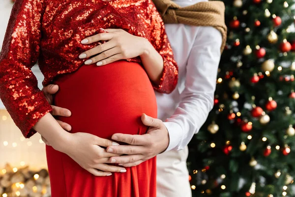 Abgeschnittene Ansicht eines Mannes, der den Bauch einer schwangeren Frau in roten und eleganten Kleidern umarmt — Stockfoto