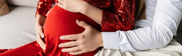 Частичный взгляд мужчины, обнимающего животик беременной жены в элегантной одежде, баннер — стоковое фото