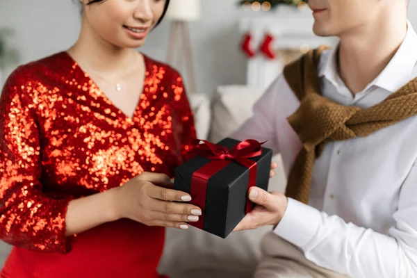 Partial view of pregnant woman in red and shiny clothing taking Christmas present from husband — Stock Photo
