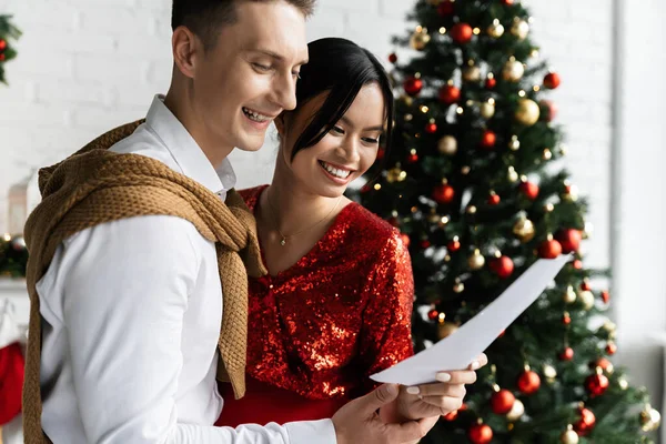Incinta asiatico donna con felice marito guardando scheda vicino decorato albero di Natale — Foto stock