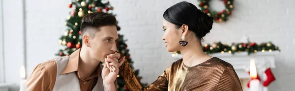 Young man kissing hand of elegant asian wife in living room during Christmas celebration, banner — Stock Photo