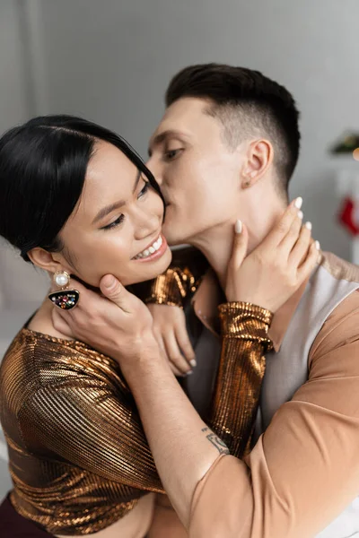 Молодой человек целуется и обнимает счастливую азиатскую жену в элегантной блузке — стоковое фото