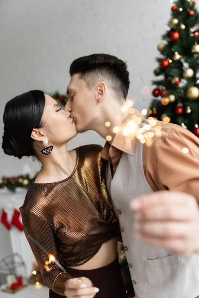 Elegant interracial couple holding festive sparklers and kissing with closed eyes — Stock Photo