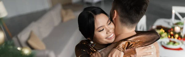 High angle view of cheerful asian woman hugging husband during Christmas celebration, banner — Stock Photo