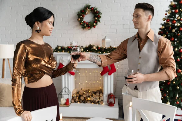 Tätowierter Mann schenkt glücklicher asiatischer Frau während Weihnachtsfeier ein Glas Wein — Stockfoto