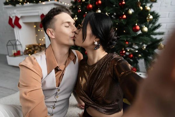 Couple interracial avec les yeux fermés baisers tout en étant assis sous l'arbre de Noël — Photo de stock