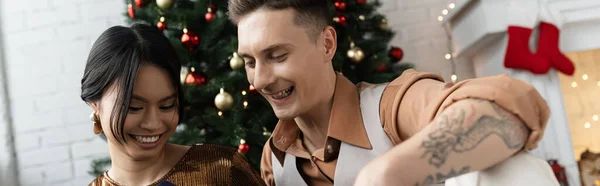 Счастливая женщина и татуированный мужчина у рождественской елки дома, баннер — стоковое фото