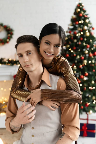 Cheerful asian woman hugging husband near decorated Christmas tree — Stock Photo