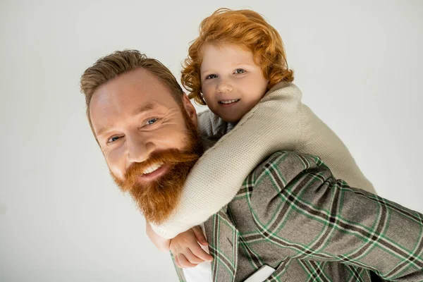 Ragazzo rosso che abbraccia il papà barbuto e guarda la fotocamera isolata sul grigio — Foto stock