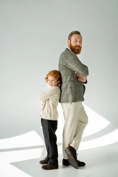 Stylish redhead boy standing back to back with dad on grey background — Stock Photo