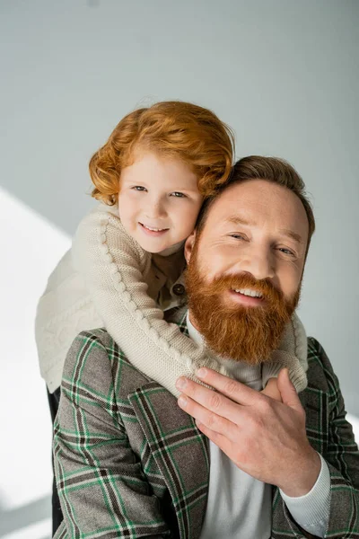 Garçon rousse en pull tricoté embrassant papa barbu sur fond gris — Photo de stock