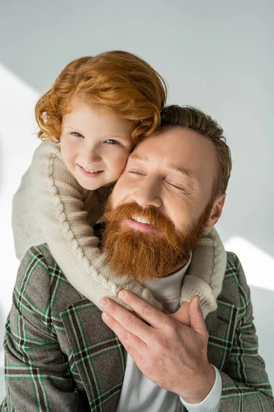 Positivo pelirrojo chico abrazando barbudo padre en chaqueta sobre fondo gris - foto de stock