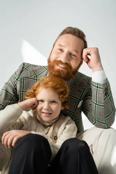 Retrato de pai na moda e menino de cabelos vermelhos olhando para a câmera no fundo cinza com luz — Fotografia de Stock