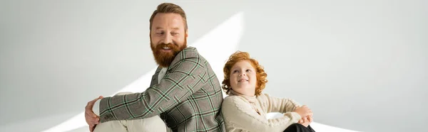 Cheerful red haired man in warm jumper looking at bearded parent on grey background with light, banner — Stock Photo