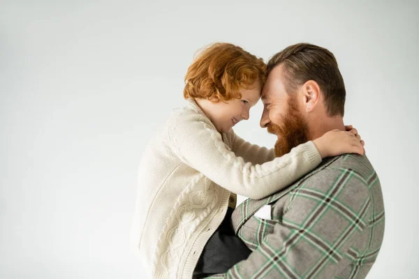 Vista laterale del bambino dai capelli rossi sorridente abbracciando papà elegante isolato sul grigio — Foto stock