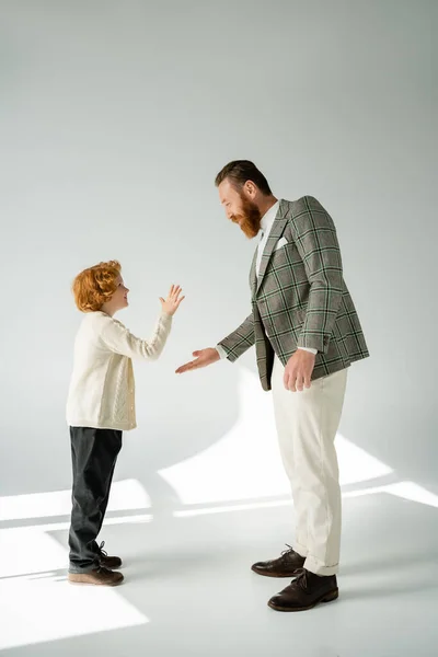 Side view of smiling redhead boy and father giving low five on grey background — Stock Photo