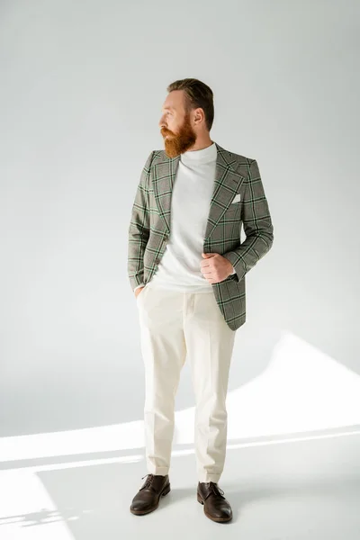 Vista laterale dell'uomo elegante e barbuto che distoglie lo sguardo su sfondo grigio con luce solare — Foto stock