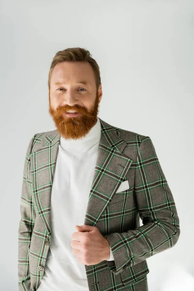 Портрет стильного бородатого чоловіка в картатій куртці, який дивиться на камеру на сірому фоні — стокове фото