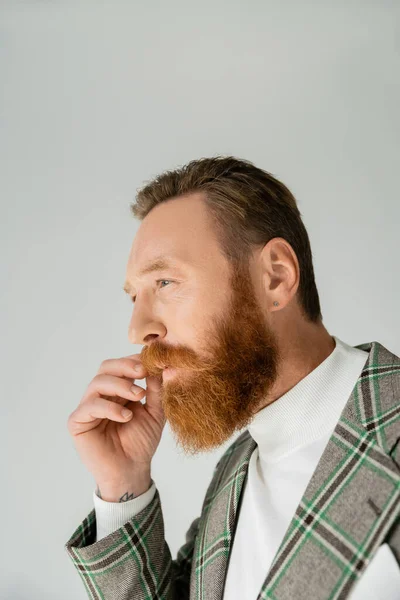 Портрет бородатого мужчины в клетчатой куртке касающихся усов, изолированных на сером — стоковое фото