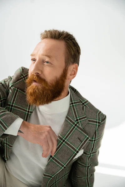 Bearded man in checkered jacket looking away on grey background with light — Stock Photo