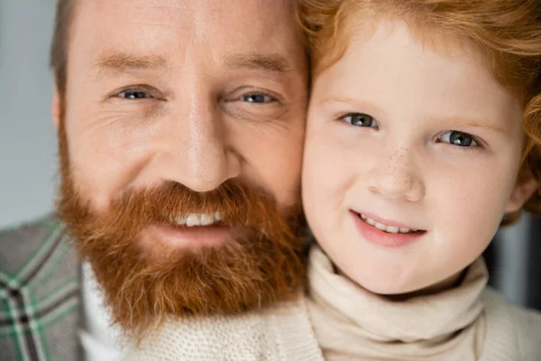 Portrait de garçon rousse souriant à la caméra près de papa barbu sur fond gris — Photo de stock