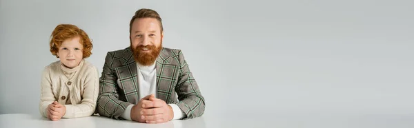Smiling bearded man in plaid jacket looking at camera near red haired child isolated on grey, banner — Stock Photo