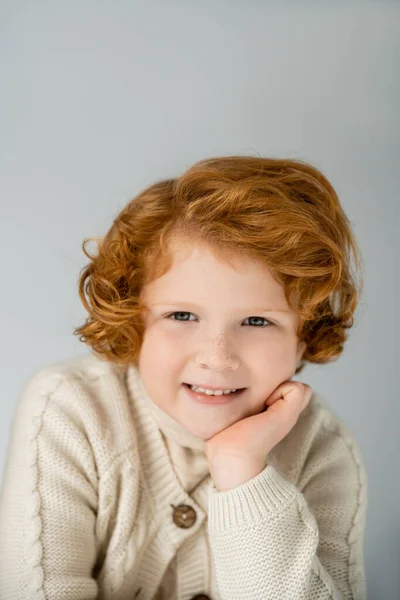 Ritratto di ragazzo rosso sorridente in maglione lavorato a maglia che guarda la macchina fotografica isolata su grigio — Foto stock