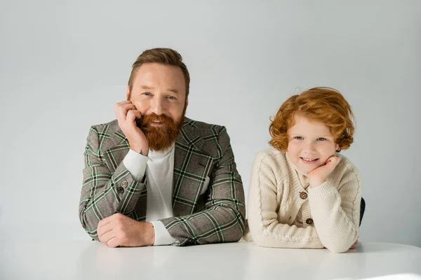 Smiling redhead child and father looking at camera near table isolated on grey — Stock Photo