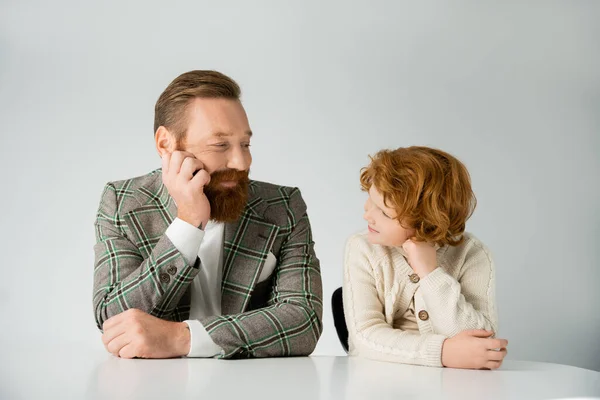 Positive bearded father and redhead son looking at each other isolated on grey — Stock Photo