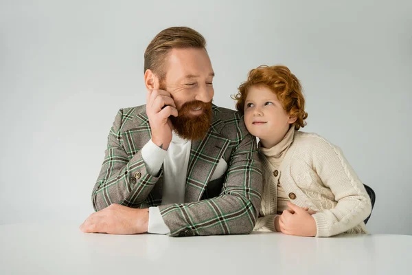 Redhead boy in jumper looking at positive dad isolated on grey — Stock Photo