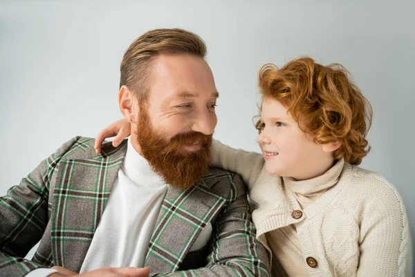 Ragazzo rosso che abbraccia e guarda papà alla moda isolato sul grigio — Foto stock