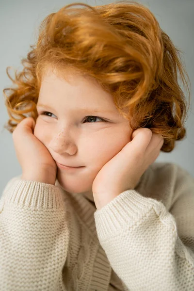 Ritratto di bambino dai capelli rossi in maglione beige lavorato a maglia distogliendo lo sguardo isolato sul grigio — Foto stock