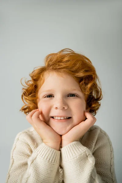 Red haired kid in warm knitted jumper smiling at camera isolated on grey — Stock Photo