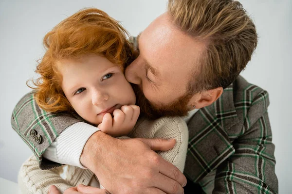 Бородатий батько цілує червоного волохатого сина в бежевому джемпері ізольовано на сірому — стокове фото