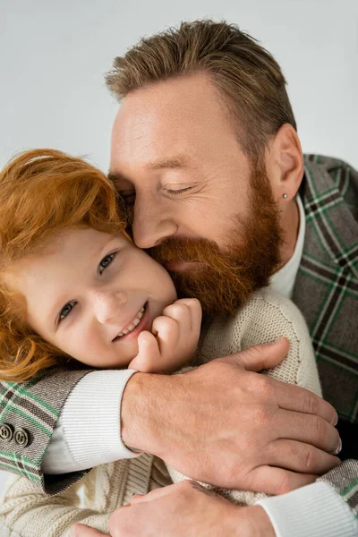 Hombre agradable y barbudo abrazando al hijo pelirrojo aislado en gris - foto de stock