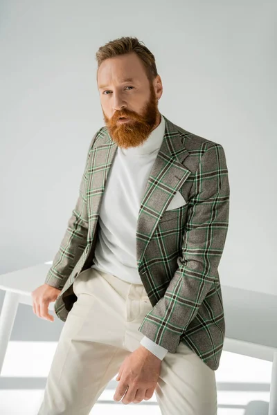 Uomo alla moda in giacca posa vicino al tavolo su sfondo grigio con luce solare — Foto stock