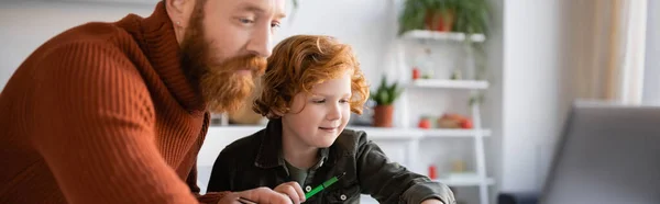 Бородатий чоловік допомагає рудому синові робити домашнє завдання, банер — стокове фото