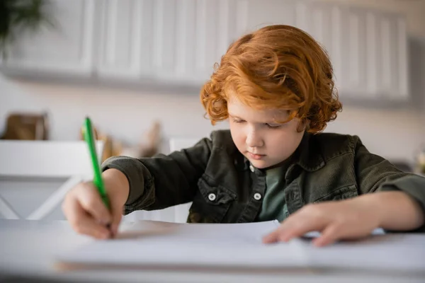 Сфокусированный мальчик с рыжими волосами делает домашнее задание и пишет размытым блокнотом — стоковое фото