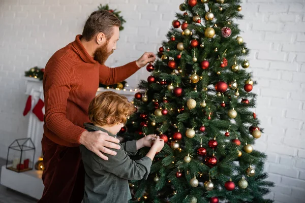 Redhead kid with bearded father decorating Christmas tree in living room at home — Stock Photo