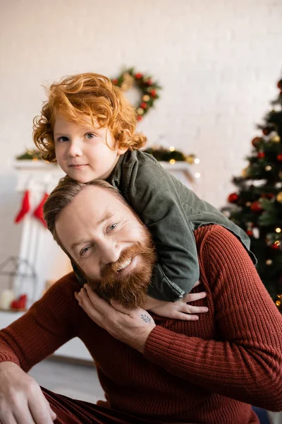 Веселый бородатый мужчина играет с рыжим сыном во время празднования Рождества — стоковое фото