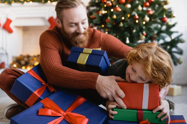 Cheerful bearded man and redhead child having fun with Christmas gift boxes at home — Stock Photo