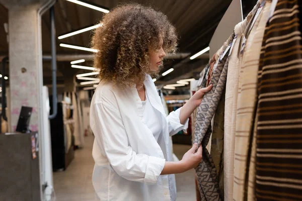 Vista lateral da vendedora encaracolado verificando material de tecido na loja têxtil — Fotografia de Stock