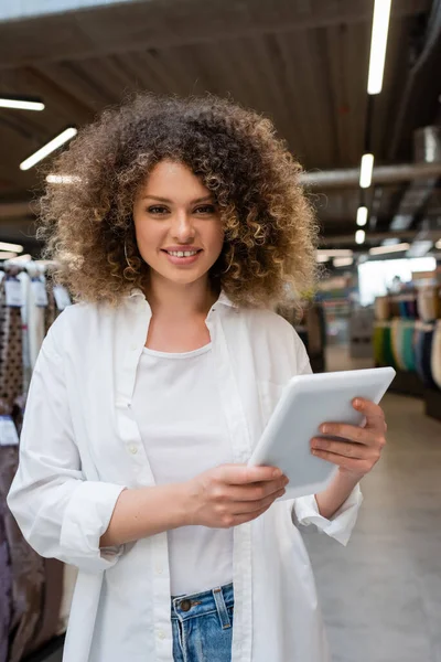 Счастливая продавщица улыбается, держа в руках цифровой планшет в текстильном магазине — стоковое фото