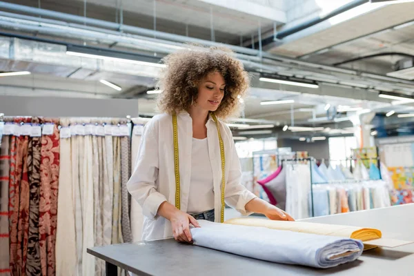 Улыбающаяся продавщица с измерительной лентой, держащая синие и желтые рулоны ткани в текстильном магазине — стоковое фото