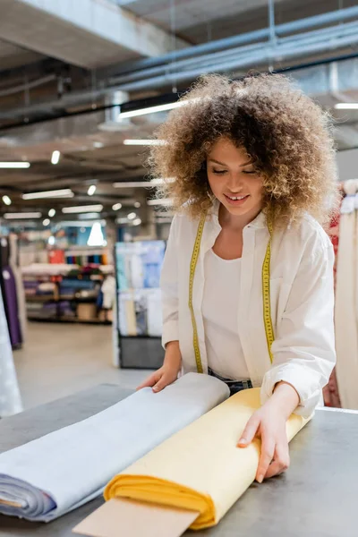 Lächelnde Verkäuferin mit Maßband zur Wahl zwischen blauen und gelben Stoffrollen — Stockfoto