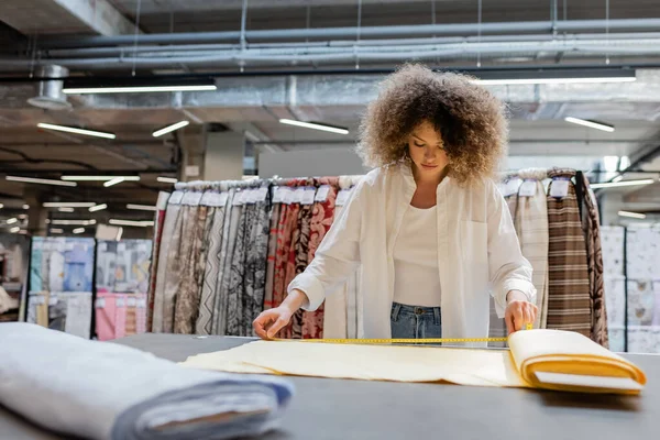 Lockige Verkäuferin misst gelbe Stoffrolle im Textilgeschäft — Stockfoto